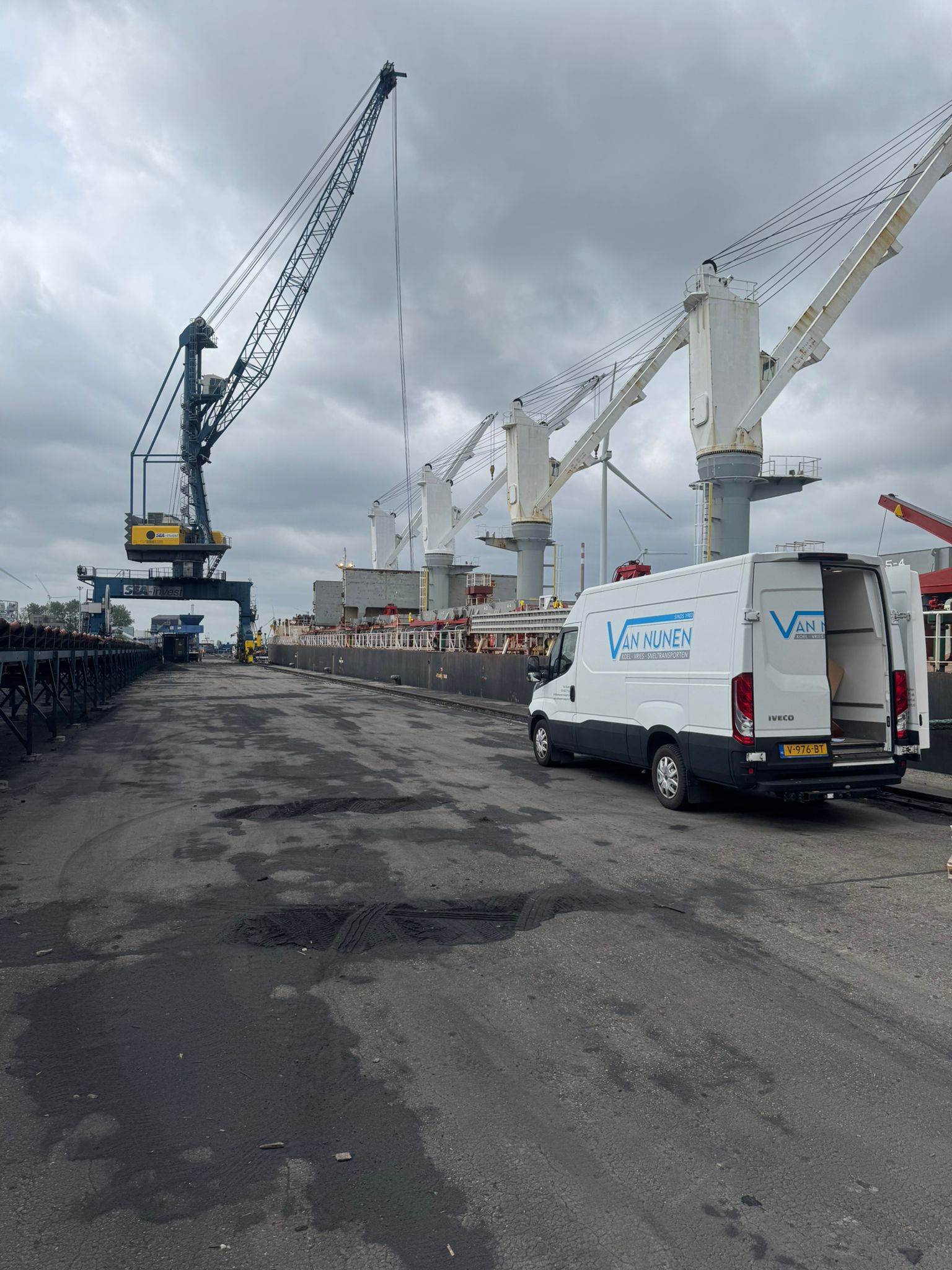Koeriersbus van de KOERIERDIENSTEN Van Nunen Transport bij een vrachtschip in de haven, klaar voor snelle levering van goederen en scheepsbelevering onder zware havenkranen.