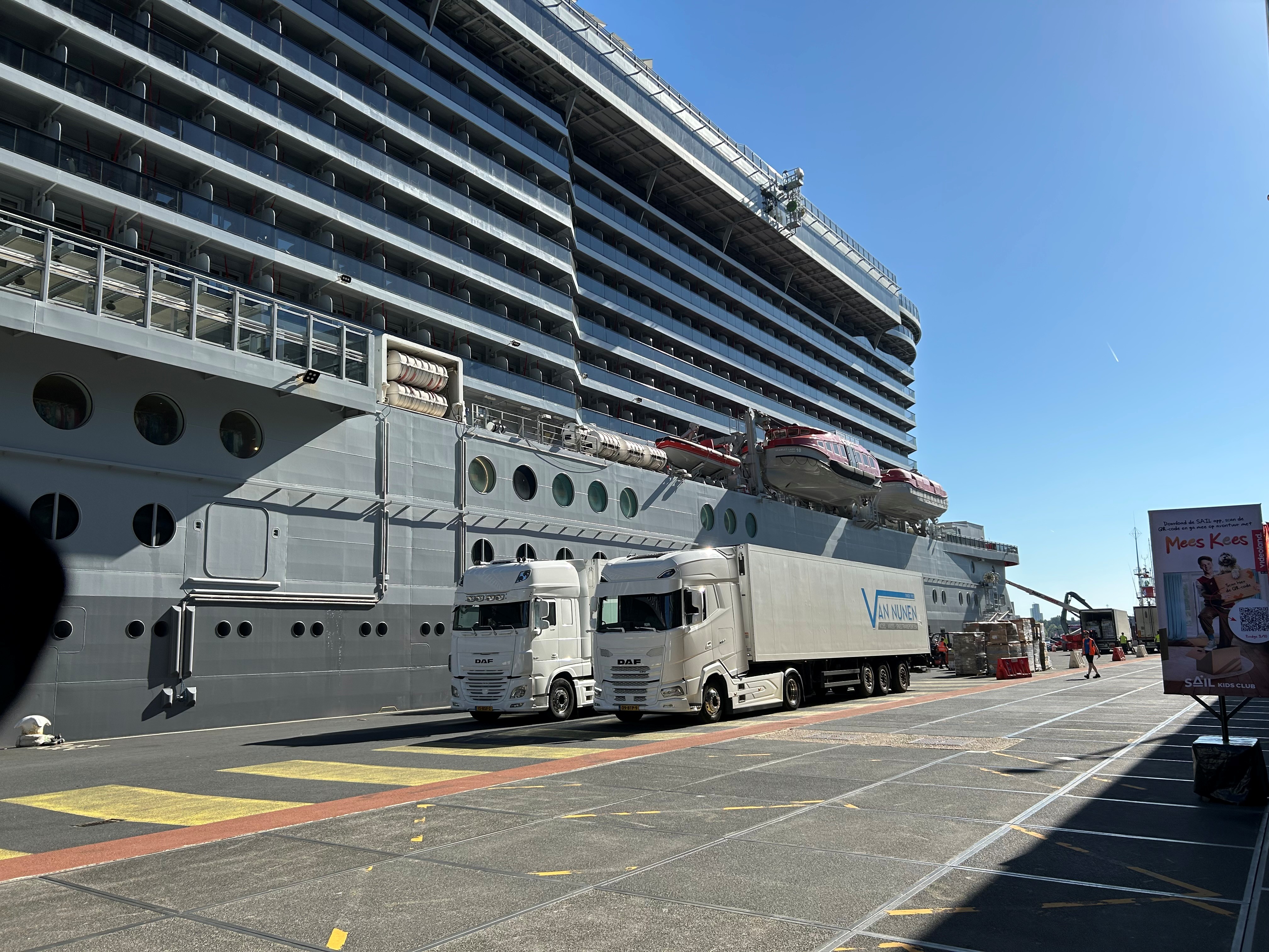 a large cruise ship with a large Van nunen truck parked on the side